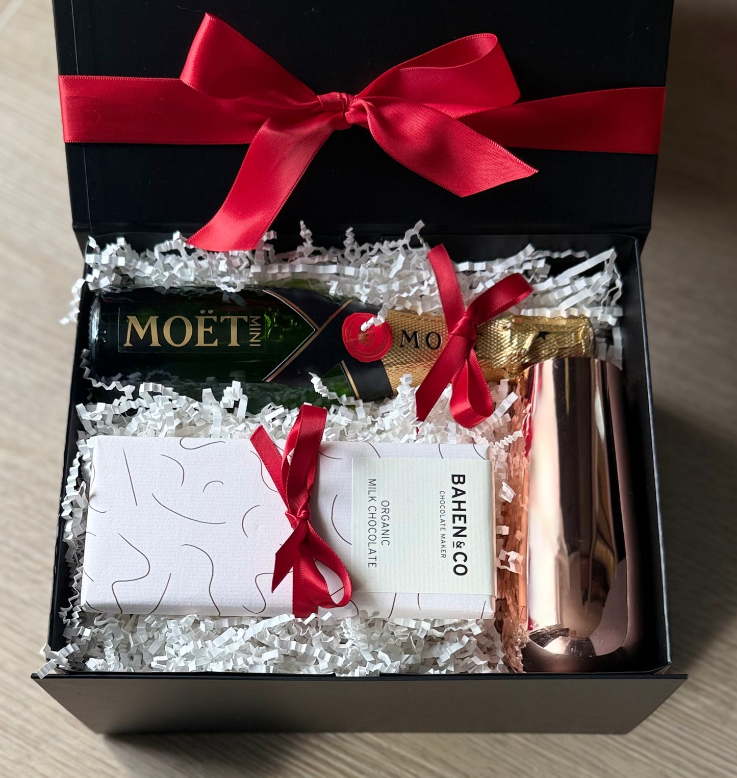 Alt text:
The Mini One gift box featuring Mini Moët & Chandon champagne, Bahen & Co chocolate, and a copper stemless flute with red ribbon packaging