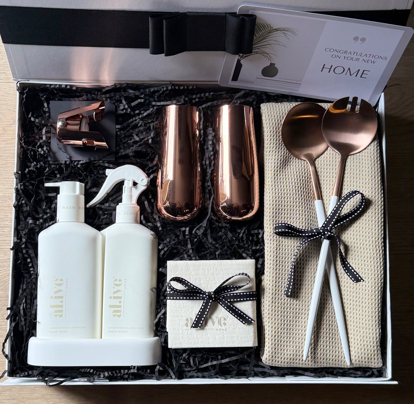Make Yourself At Home gift box with al.ive body and kitchen duo, copper Clinq champagne flutes, rose-gold salad servers, tea towel, and greeting card in luxury packaging