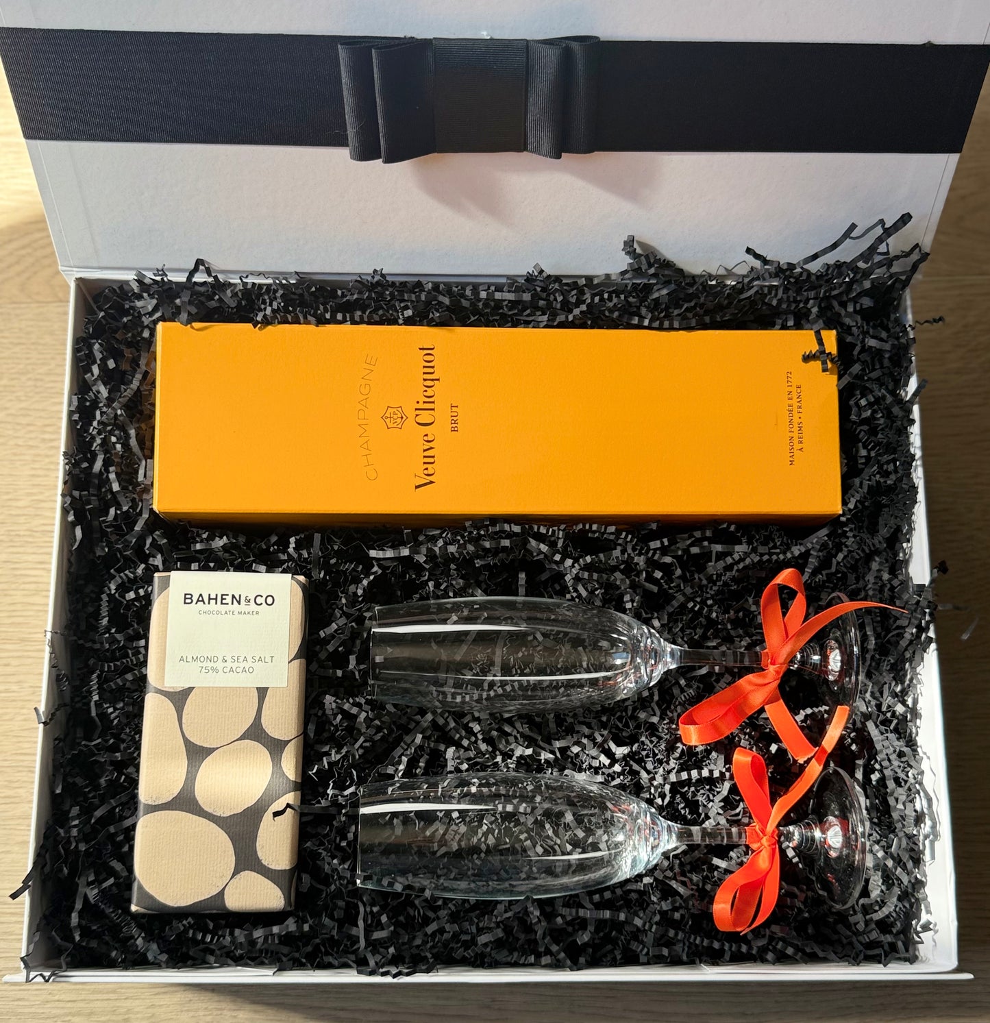 Veuve & Velvet luxury gift box with Veuve Clicquot champagne, Bahen & Co artisan chocolate, and two red-stemmed champagne flutes in elegant packaging