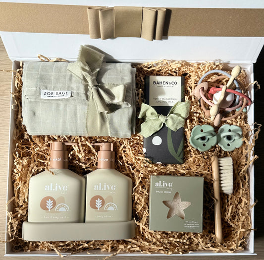 The Baby Suite gift box featuring al.ive baby Hair & Body Duo, swaddle wrap, Bahen & Co chocolate, baby brush, konjac sponge, rattle teether toy, and Bebebiu dummies on shredded paper