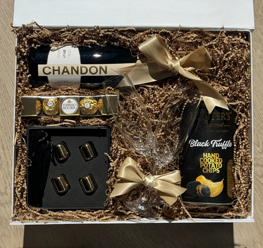 Luxury gift box featuring a bottle of Chandon Brut, Ferrero Rocher chocolates, two champagne flutes with gold bows, gold whiskey stones, and Hunter’s Gourmet Black Truffle chips, beautifully packaged.